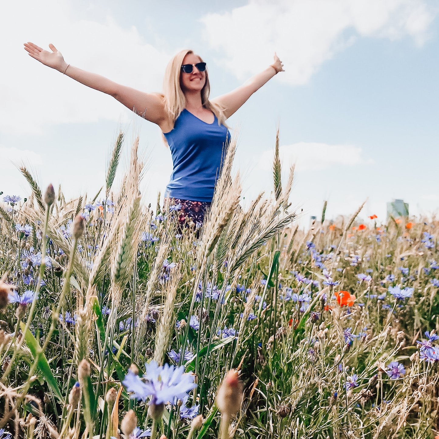 Glückliche Frau auf einer Blumenwiese (was steckt hinter deinen körperlichen Beschwerden?)